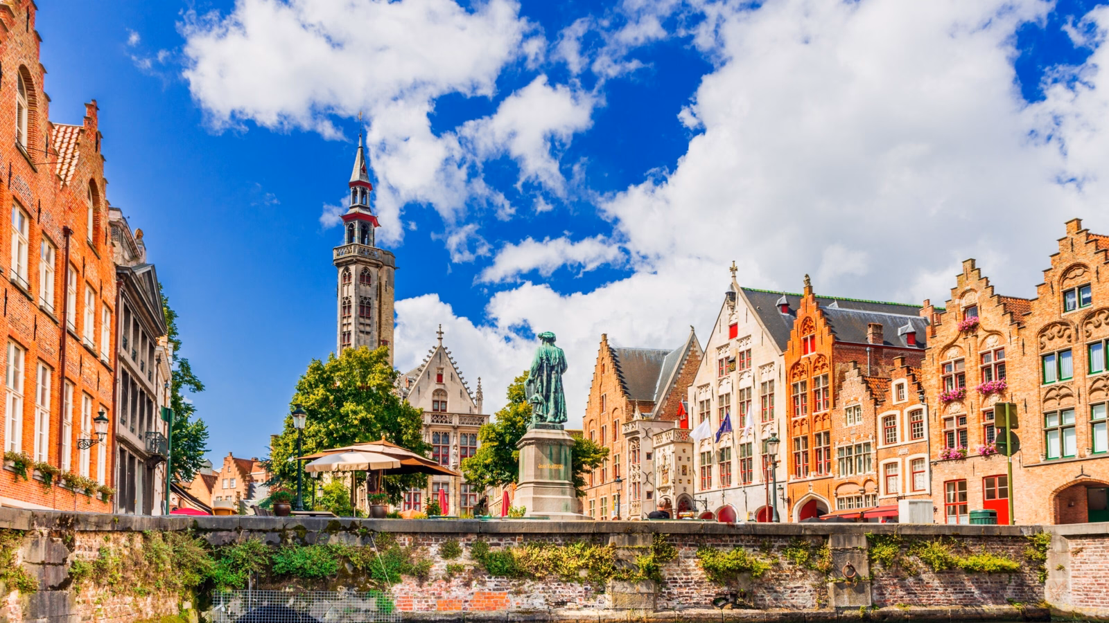 Quaint European canal with traditional buildings and a belfry under a blue sky with clouds.