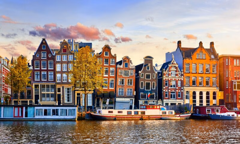 Colourful Dutch houses by a canal at sunset with a houseboat in Amsterdam.