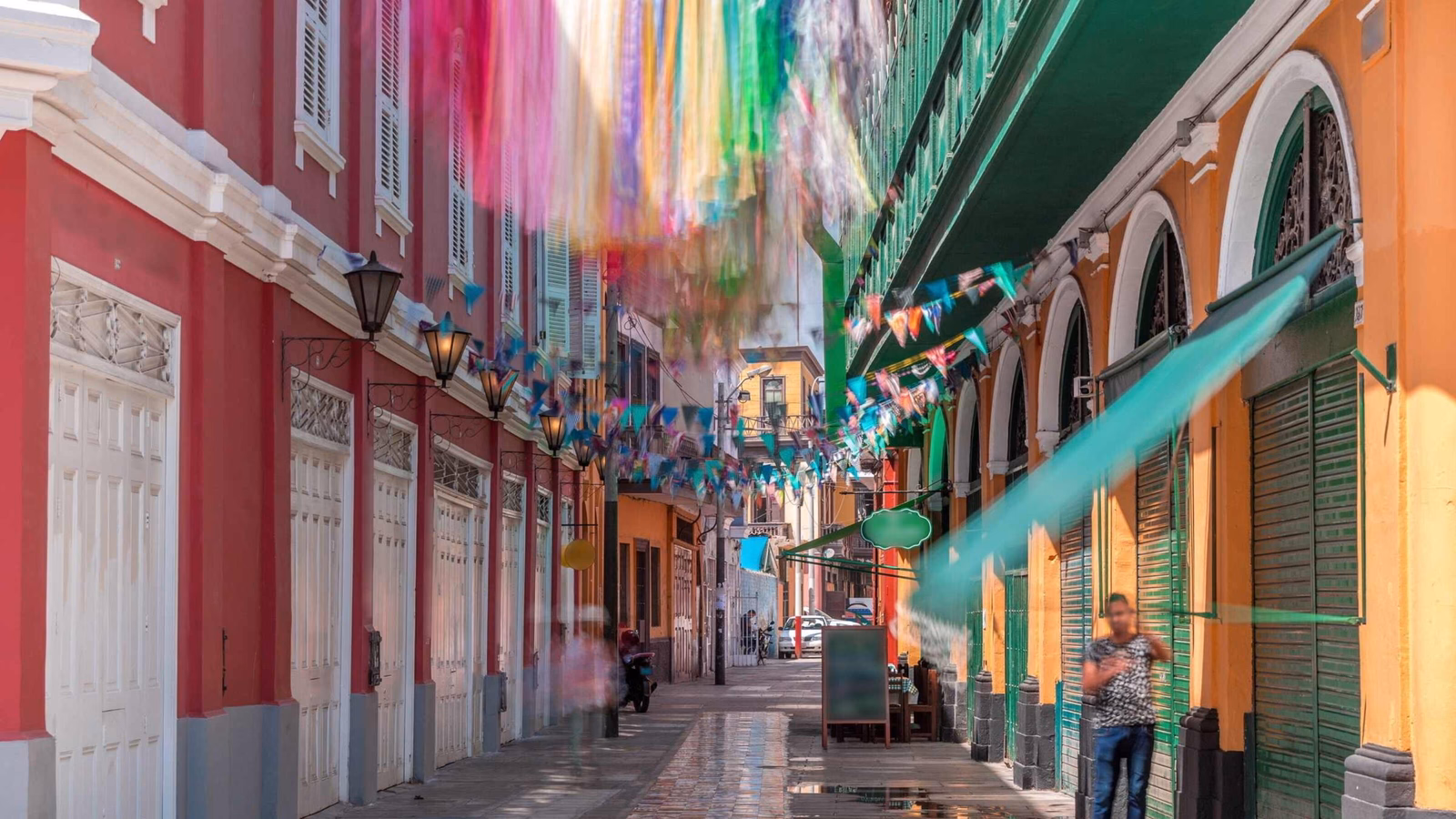 Colourful ribbons hanging above a vibrant street with colonial architecture.