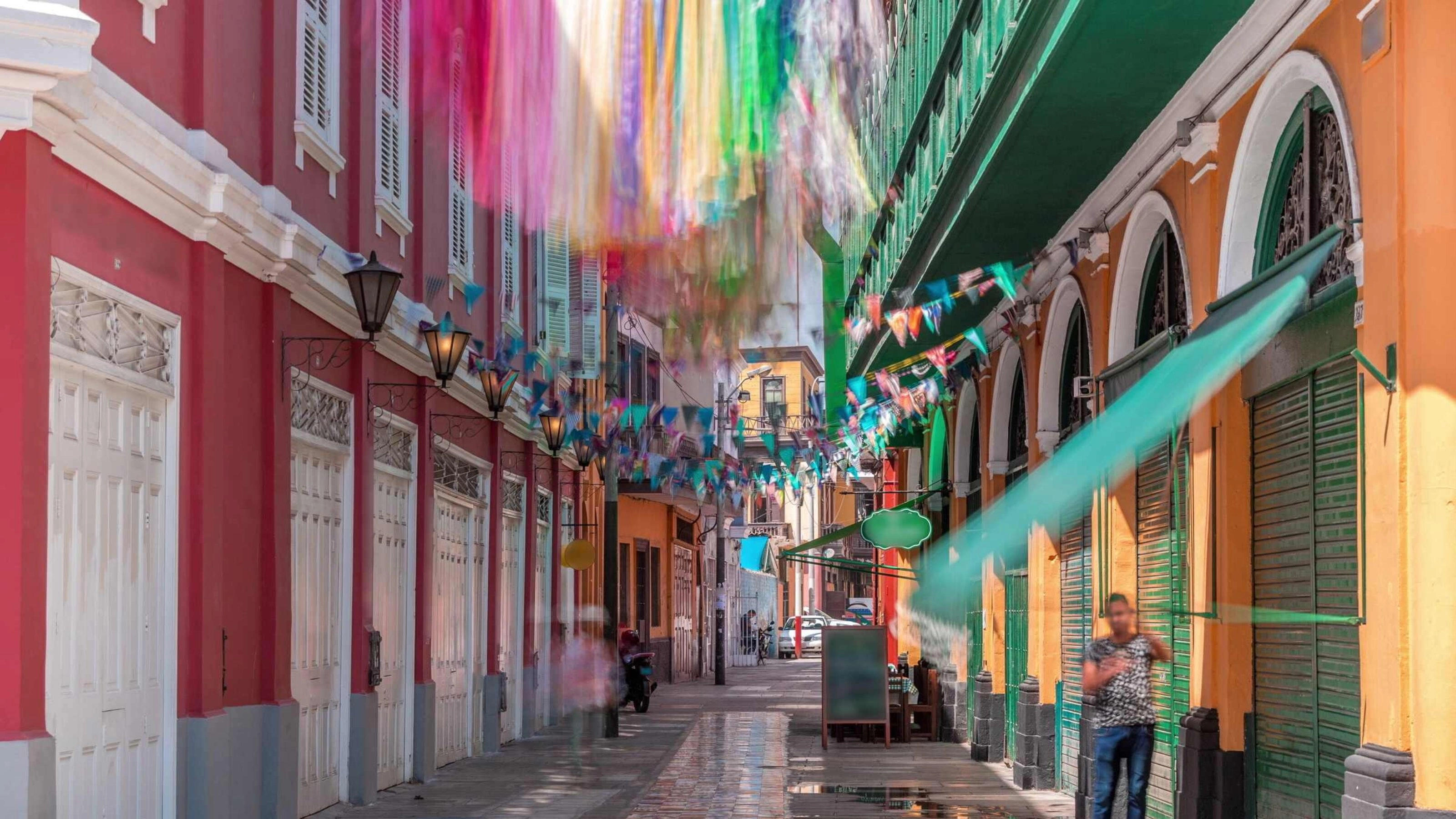 Colourful ribbons hanging above a vibrant street with colonial architecture.