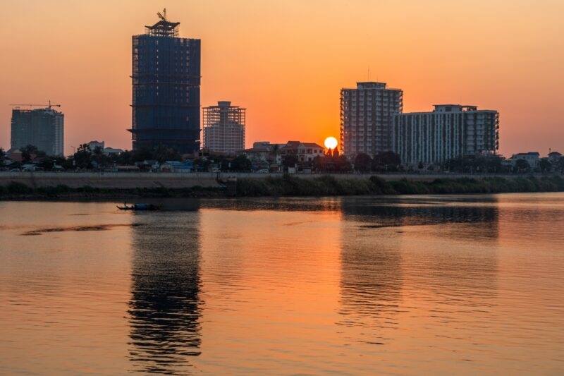 Sunset over a river with silhouette of city skyline and a small boat on the water.