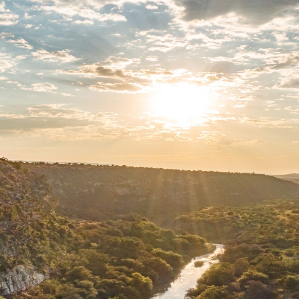 Sunset over a lush river valley with light breaking through scattered clouds.
