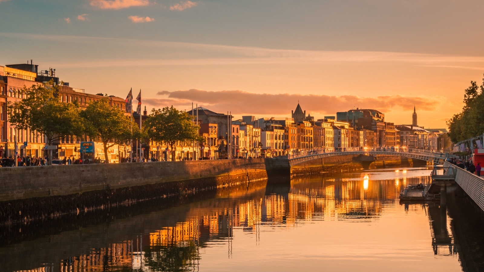Sunset over a city river with reflections, bridge in the distance, and riverside buildings.