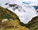 Stone terraces of an Inca ruin on a lush mountainside surrounded by clouds during luxury Inca Trail tours.