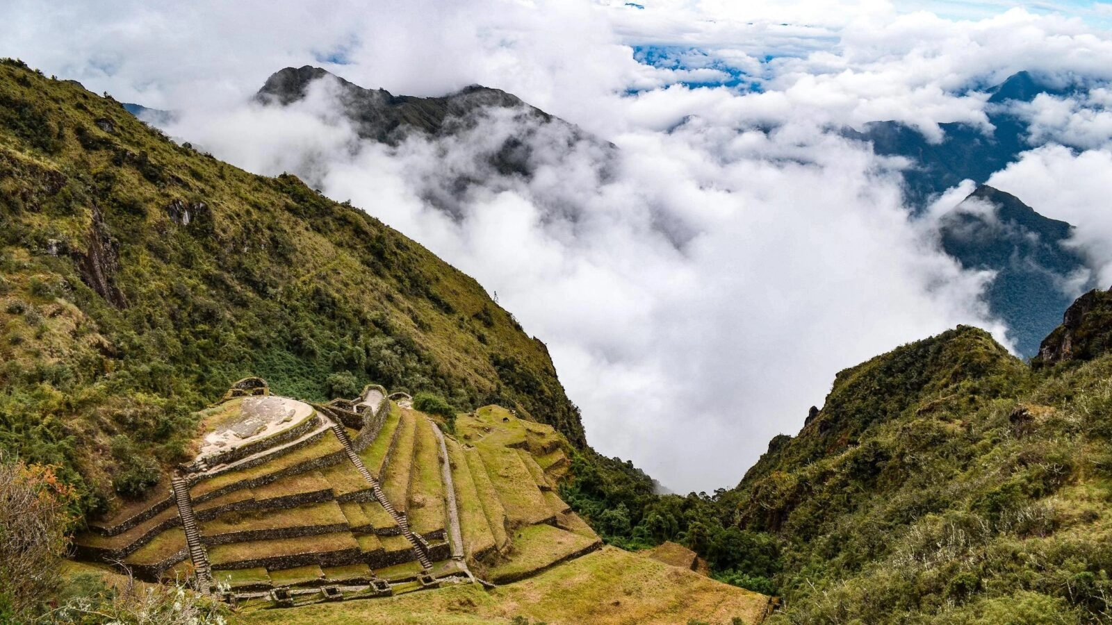 Terraced slopes of Inca citadel with clouds enveloping the surrounding Andean peaks.