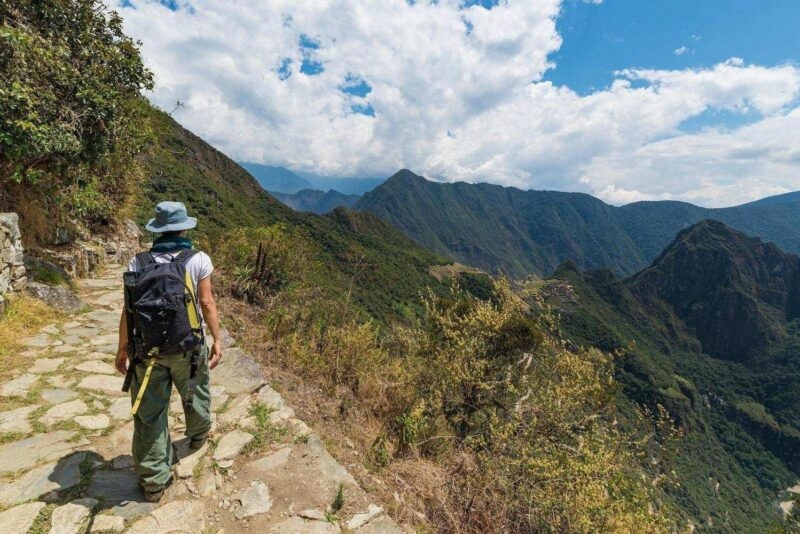 Hiker walking along a stone mountain path overlooking a vast valley during luxury Inca Trail trips.