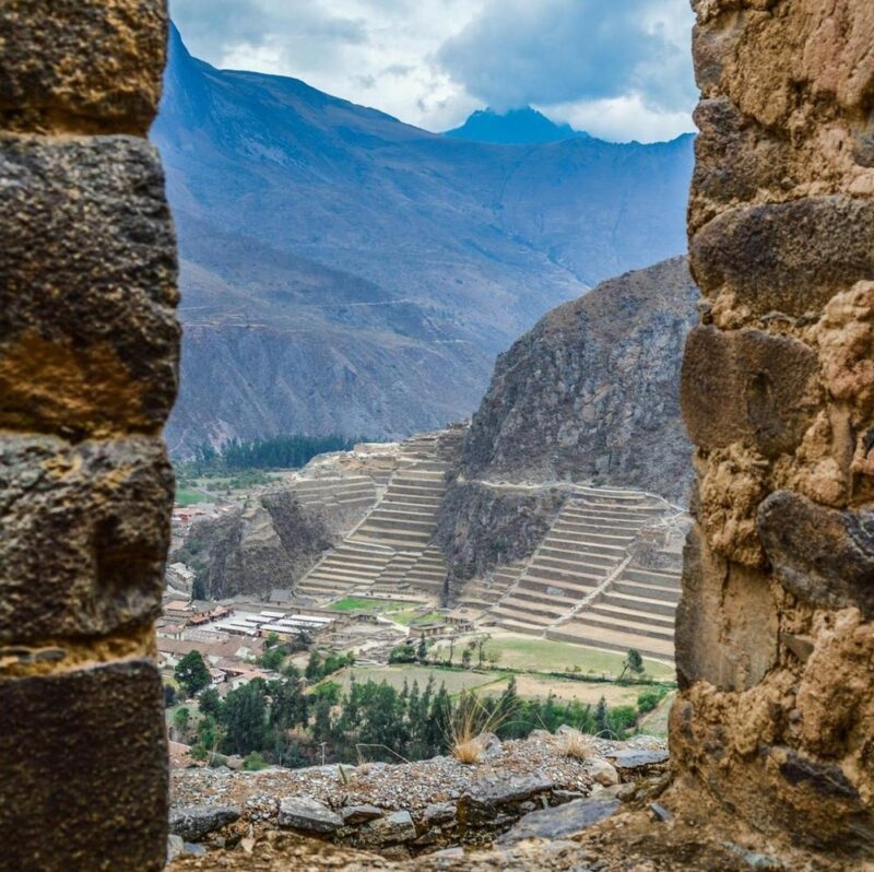 View of ancient terraces through stone ruins against a mountainous backdrop.