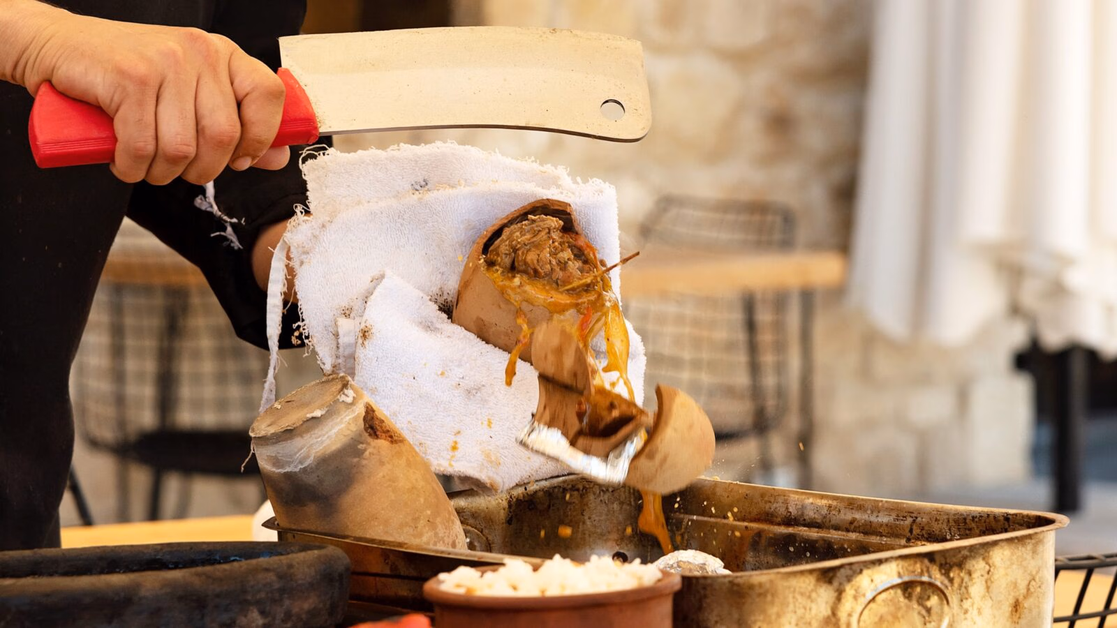 A person slicing open a cooked dish wrapped in cloth with a large knife.