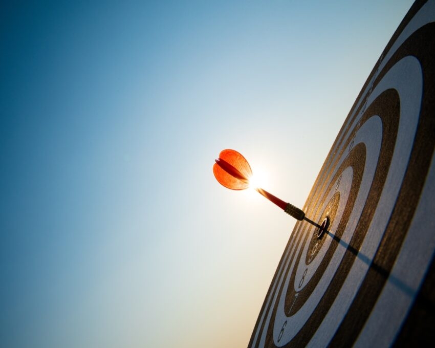 Arrow hitting bullseye on target against a clear blue sky with sun flare.