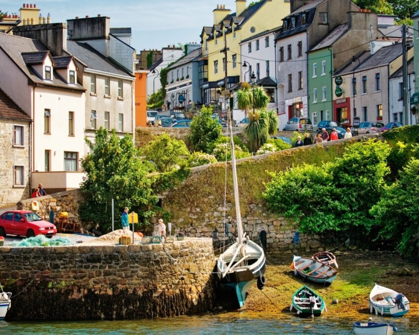 Colourful seaside town with boats docked near a stone wall, under bright sunlight.