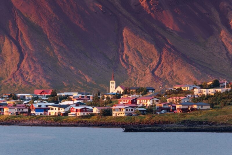 A quaint seaside village with colorful houses nestled at the base of a mountain at sunset.