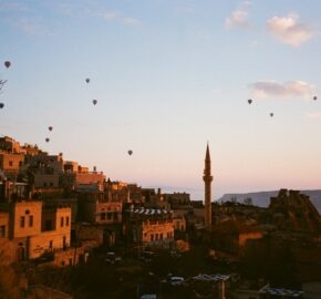 Sunset over a historic town with a mosque and hot air balloons in the sky.