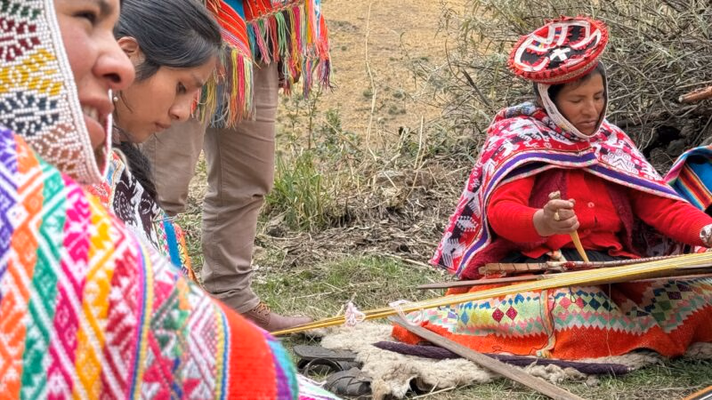 Women in colorful traditional dress weaving textiles during positive impact tours.