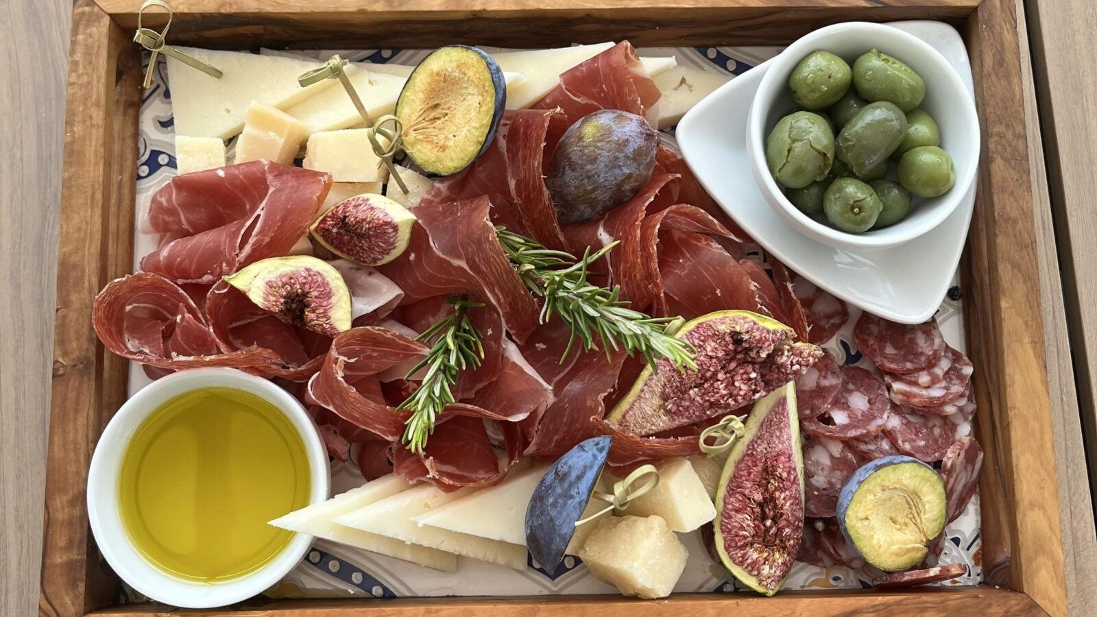 A charcuterie board with meats, cheese, figs, olives and olive oil.