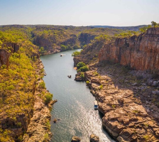 Aerial view of a river canyon with steep cliffs and boats, surrounded by greenery.