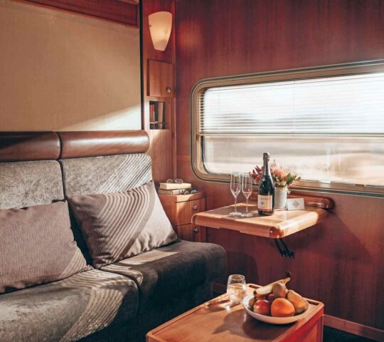 Elegant train cabin interior with sofa, table setting with wine, and window view.
