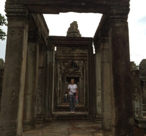 Person walking through ancient stone doorways in a historical temple complex.
