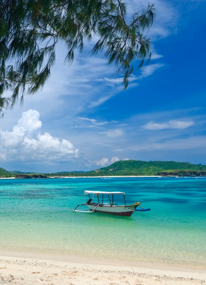 A traditional boat floats on crystal-clear turquoise waters, surrounded by lush green hills and a blue sky dotted with clouds.