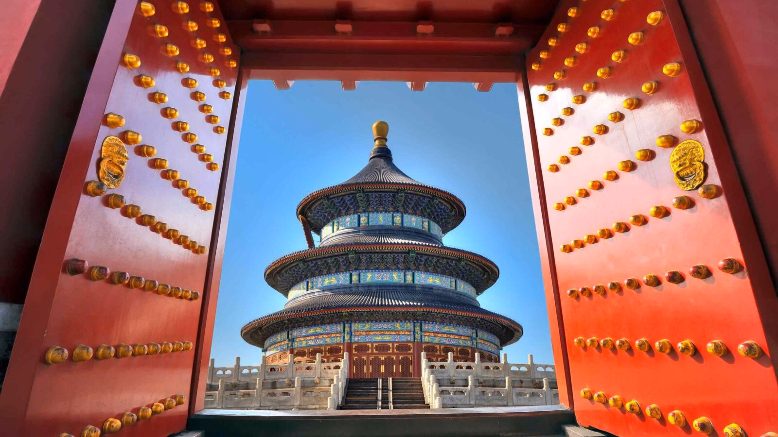 View of the Temple of Heaven through open red imperial doors with gold studs during luxury China holidays.