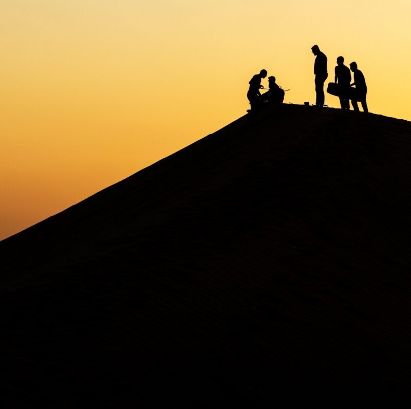 Silhouettes of five people on a steep sand dune ridge at sunset during Namibia family tours.