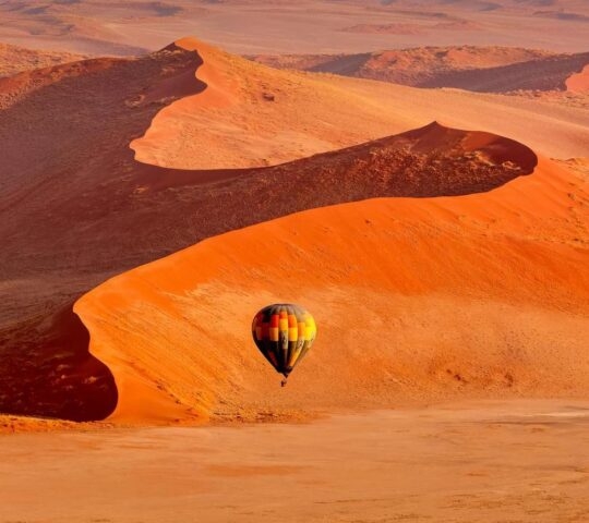 Hot air balloon in flight against orange sand dunes in Sossusvlei Namibia
