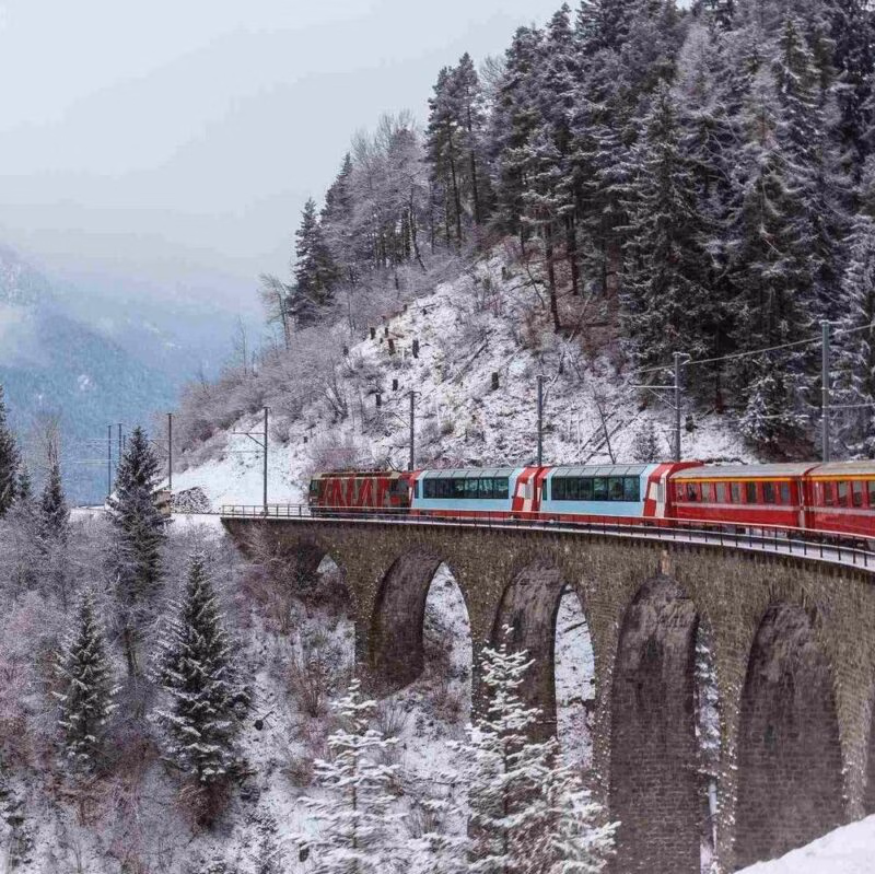 The Glacier Express train travelling across a snowy bridge in Switzerland