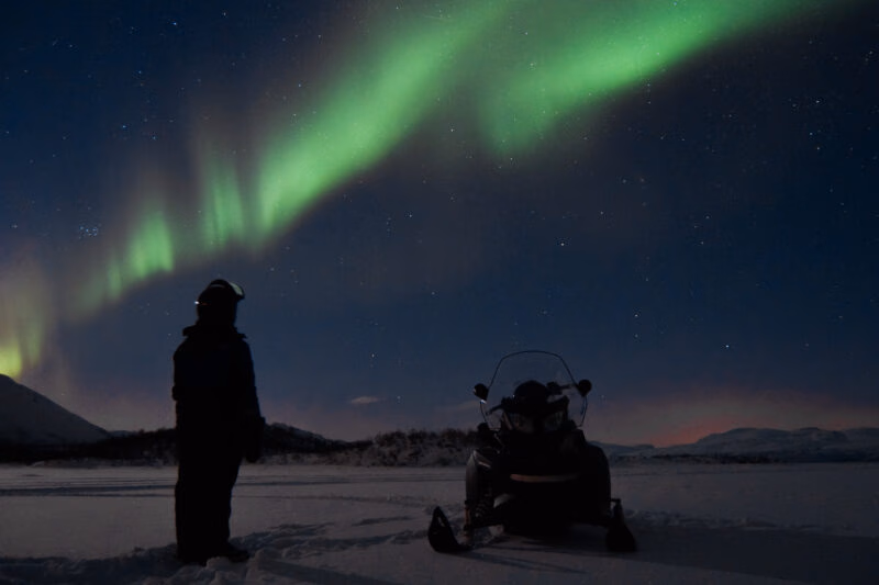 a person stood with a snowmobile watching the northern lights