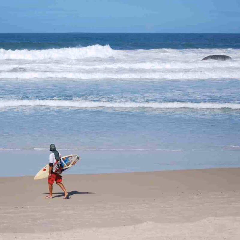 A surfer walks along the beach in Florianópolis