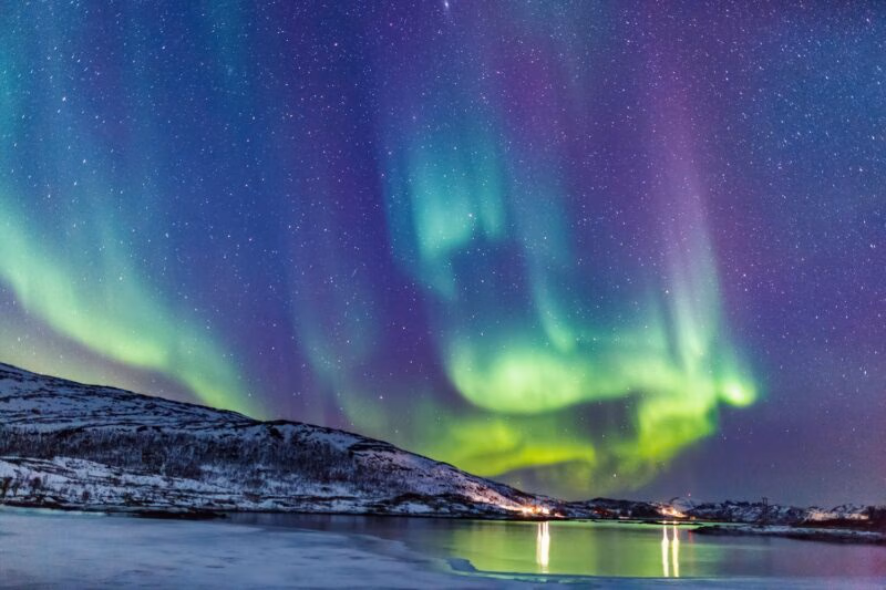 Green and purple northern lights above a mountain and lake landscape