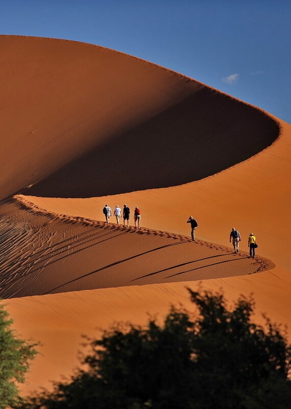 Hikers walking along the ridge of a large desert sand dune on Namibia and Botswana Luxury Safaris.