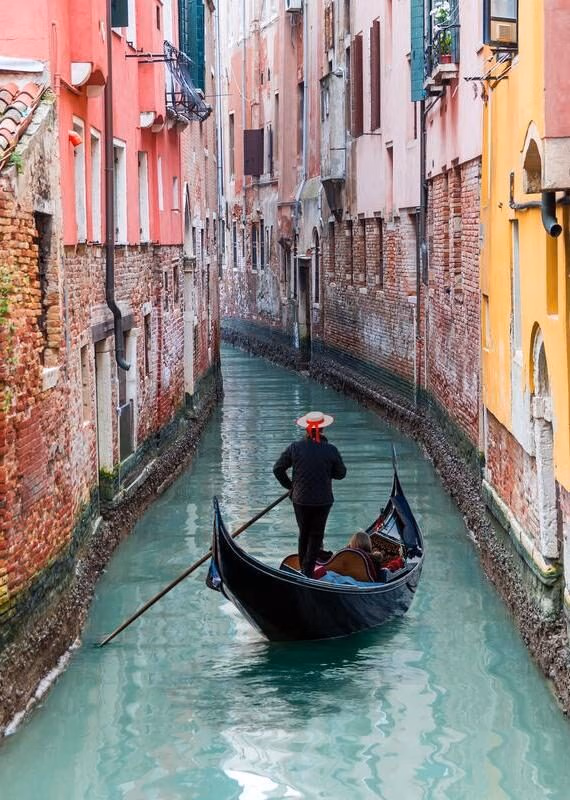 Venetian gondolier through green canal waters of Venice Italy