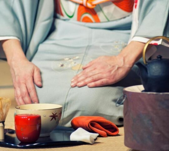 Scene from Japanese tea ceremony with a geisha kneeling on the floor next to cups