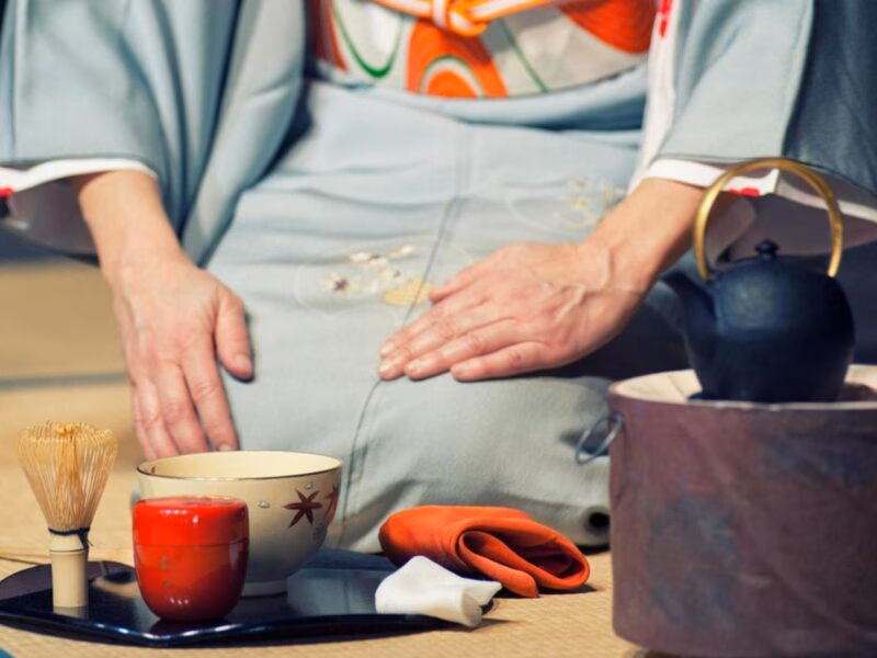 Scene from Japanese tea ceremony with a geisha kneeling on the floor next to cups