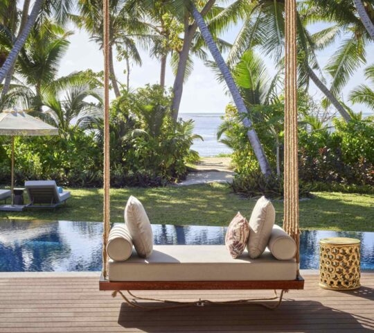 The outdoor area of a villa at Waldorf Astoria Seychelles Platte Island, featuring a pool, sun loungers in a garden and a path to the beach.