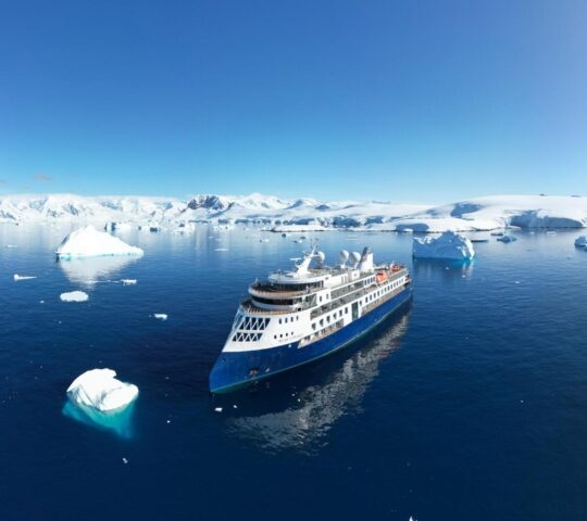 An aerial view of Ocean Explorer cruising between icebergs.