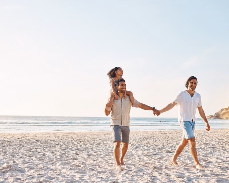 A gay couple walking on the beach with a small child