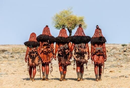 Himba women in traditional dress walking through a desert landscape on Namibia and Botswana Luxury Safaris.