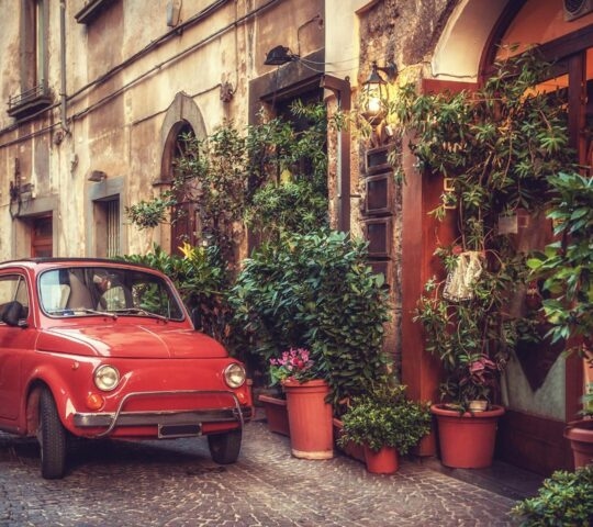 Old vintage cult car parked on the street by the restaurant, in the Italian town.