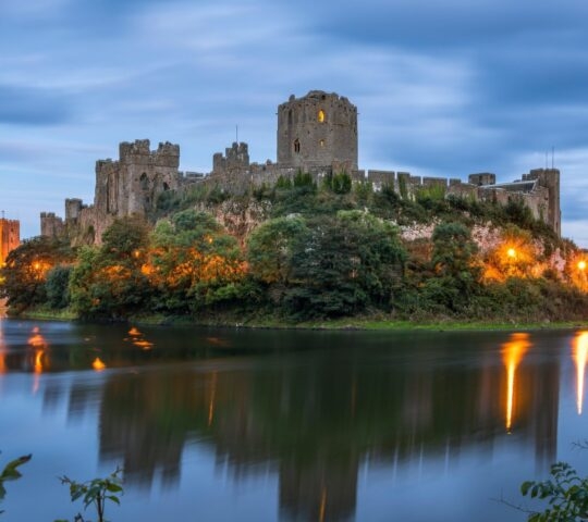 Pembroke castle illuminated at night and reflected in the river