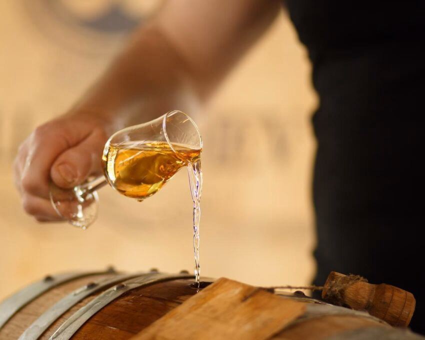 A man pouring whisky into a barrel at a whisky distillery