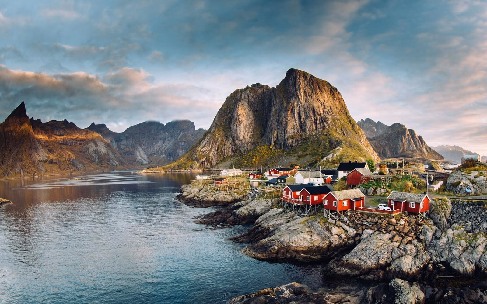 Evening light over the red fishing cabins of the Lofoten Islands with rugged peaks rising above the fjord in northern Norway.