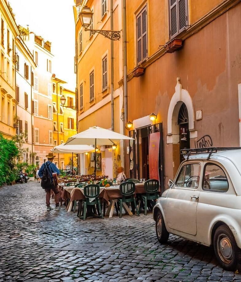 A cobblestone street lined with cafés in Rome’s Trastevere district and a glowing evening view of Florence’s skyline crowned by the Cathedral of Santa Maria del Fiore.