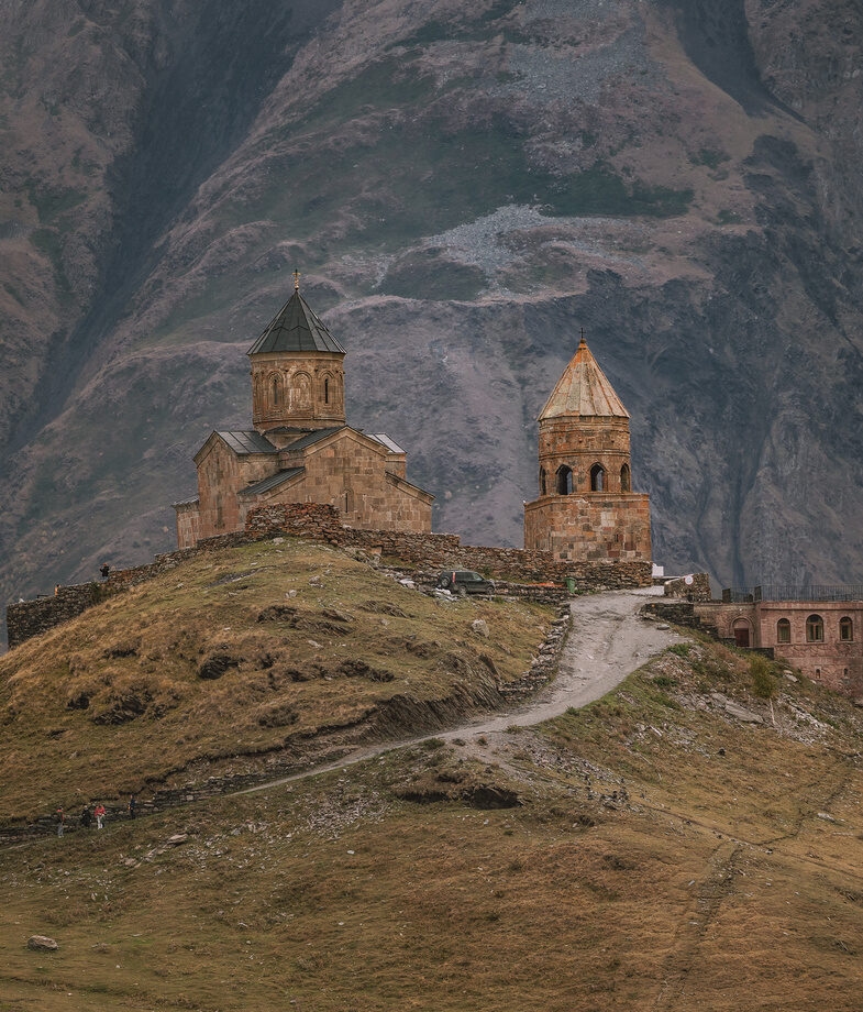 The glacial Blue Lake of Blavatnet with views of the Lyngen Alps in northern Norway and the hilltop Gergeti Trinity Church in Kazbegi National Park, Georgia.