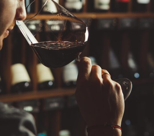 A close-up shot of a person smelling red wine with a wine cellar background.