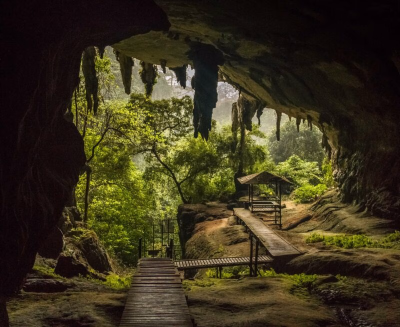 Wooden walkway and small hut inside a dark cave overlooking a bright green jungle on luxury Borneo tours.