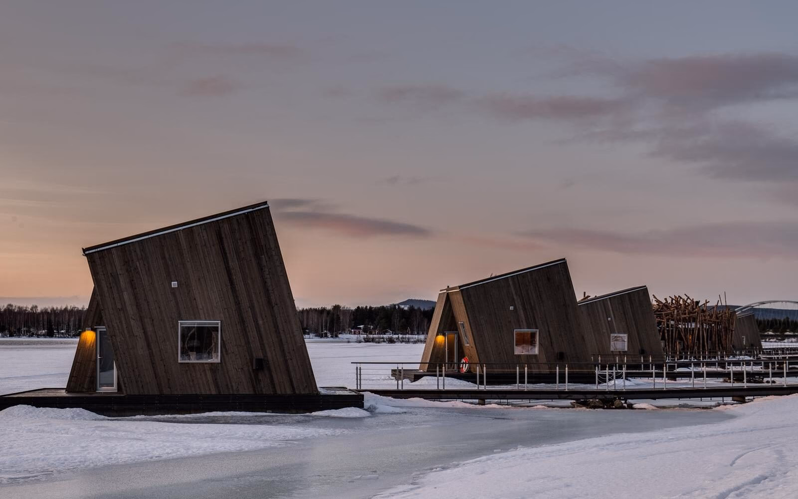 The floating wooden cabins of Arctic Bath in Sweden resting on a frozen river under soft winter light.
