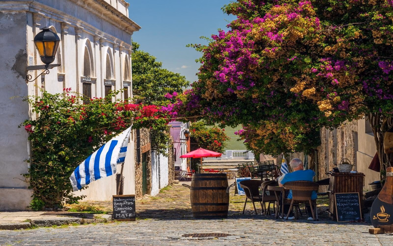 The historic city of Colonia del Sacramento, Uruguay, where some cafés are draped in vibrant bougainvillea blossoms along a cobbled street.
