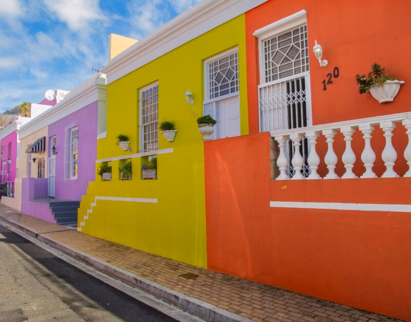 Brightly painted yellow, orange, and purple houses on a street during luxury Cape Town trips.