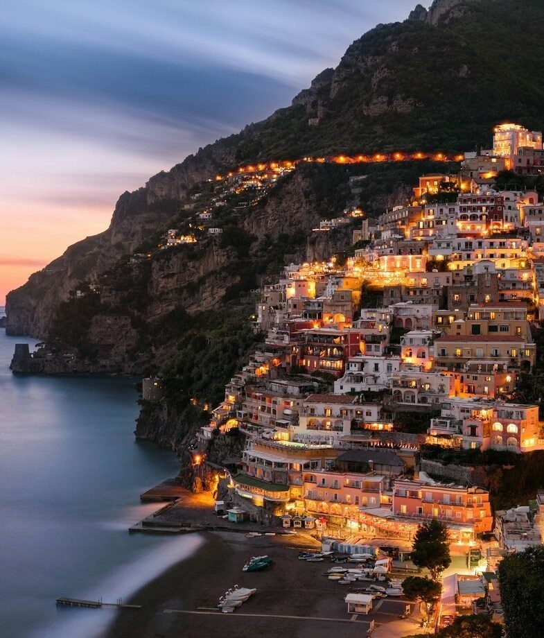 The dramatic cliffs of the Amalfi Coast glowing at dusk in Italy, and lanterns above Seville’s Feria de Abril, a traditional April celebration in Spain.