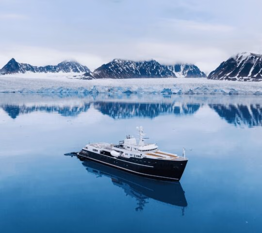An aerial of Aqua Lares cruising across the water with snowy mountains in the background.